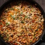orzo puttanesca in the pan after melting the cheese and topping with herbs and black pepper