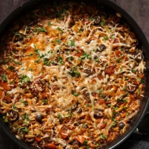 orzo puttanesca in the pan after melting the cheese and topping with herbs and black pepper