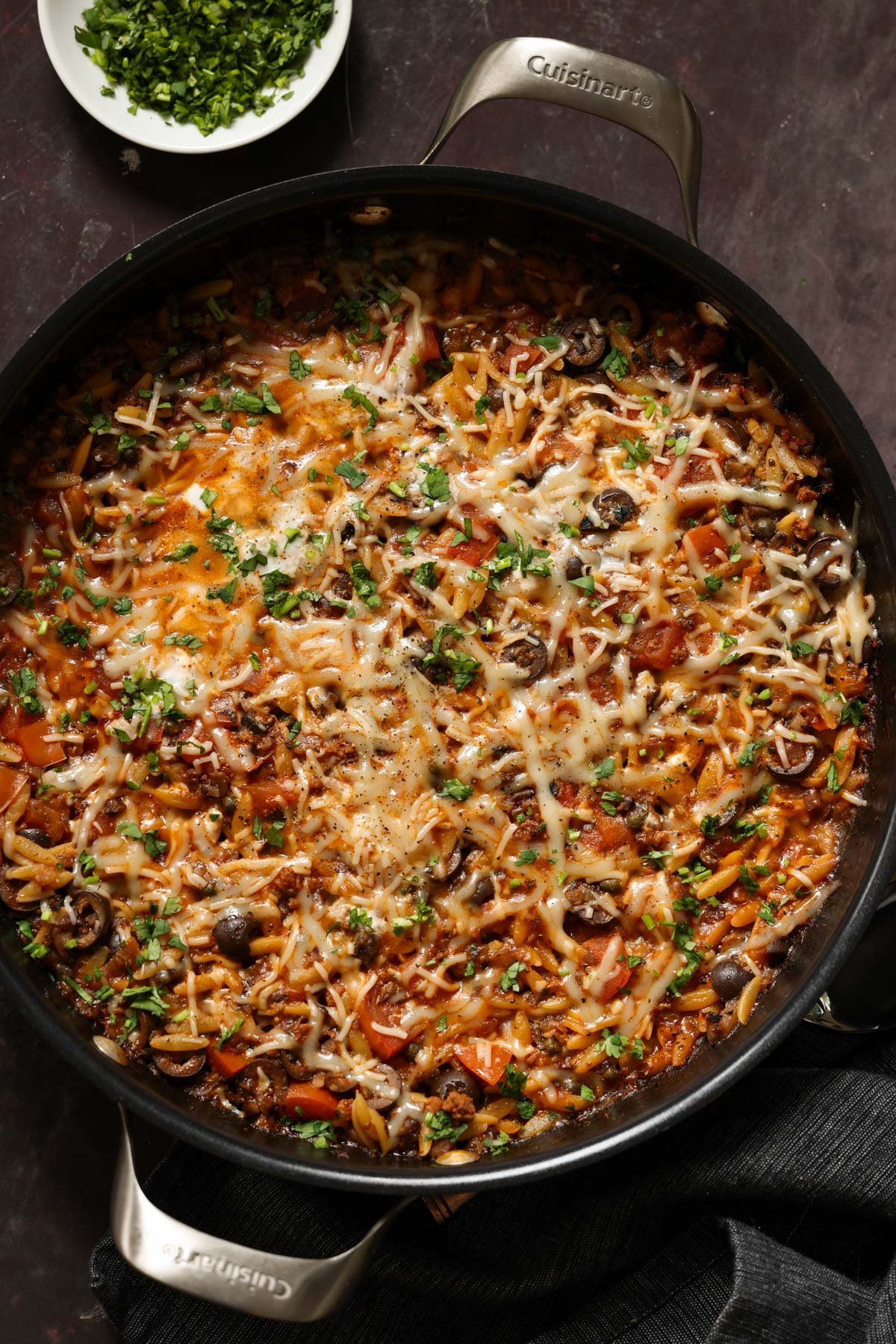 orzo puttanesca in the pan after melting the cheese and topping with herbs and black pepper