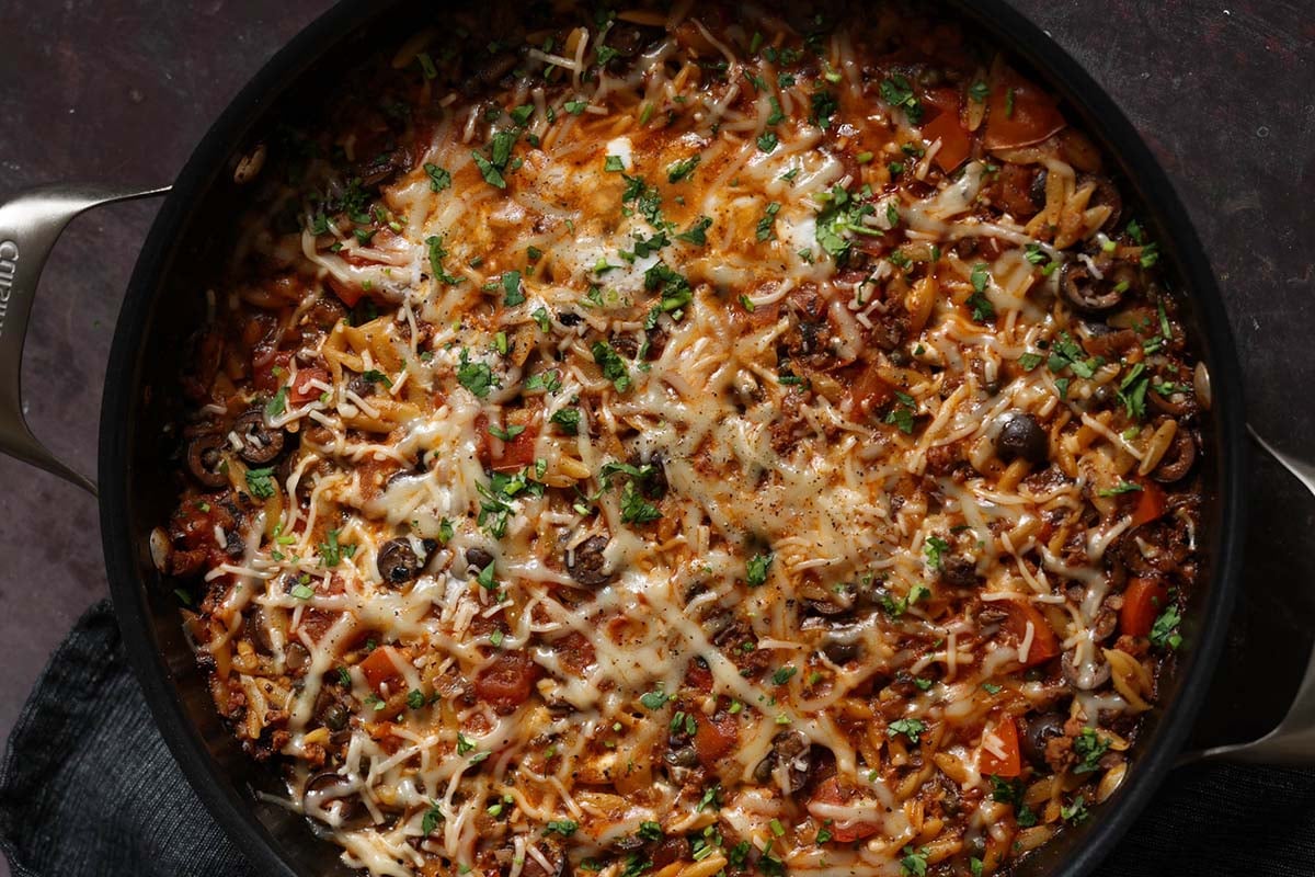 orzo puttanesca in the pan after melting the cheese and topping with herbs and black pepper