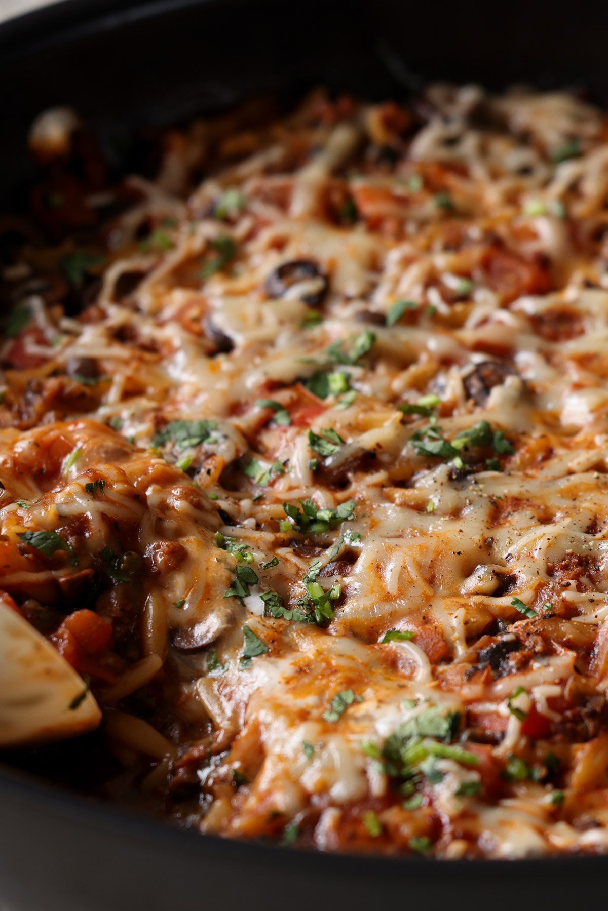 close-up of scooping up some orzo puttanesca from the pan