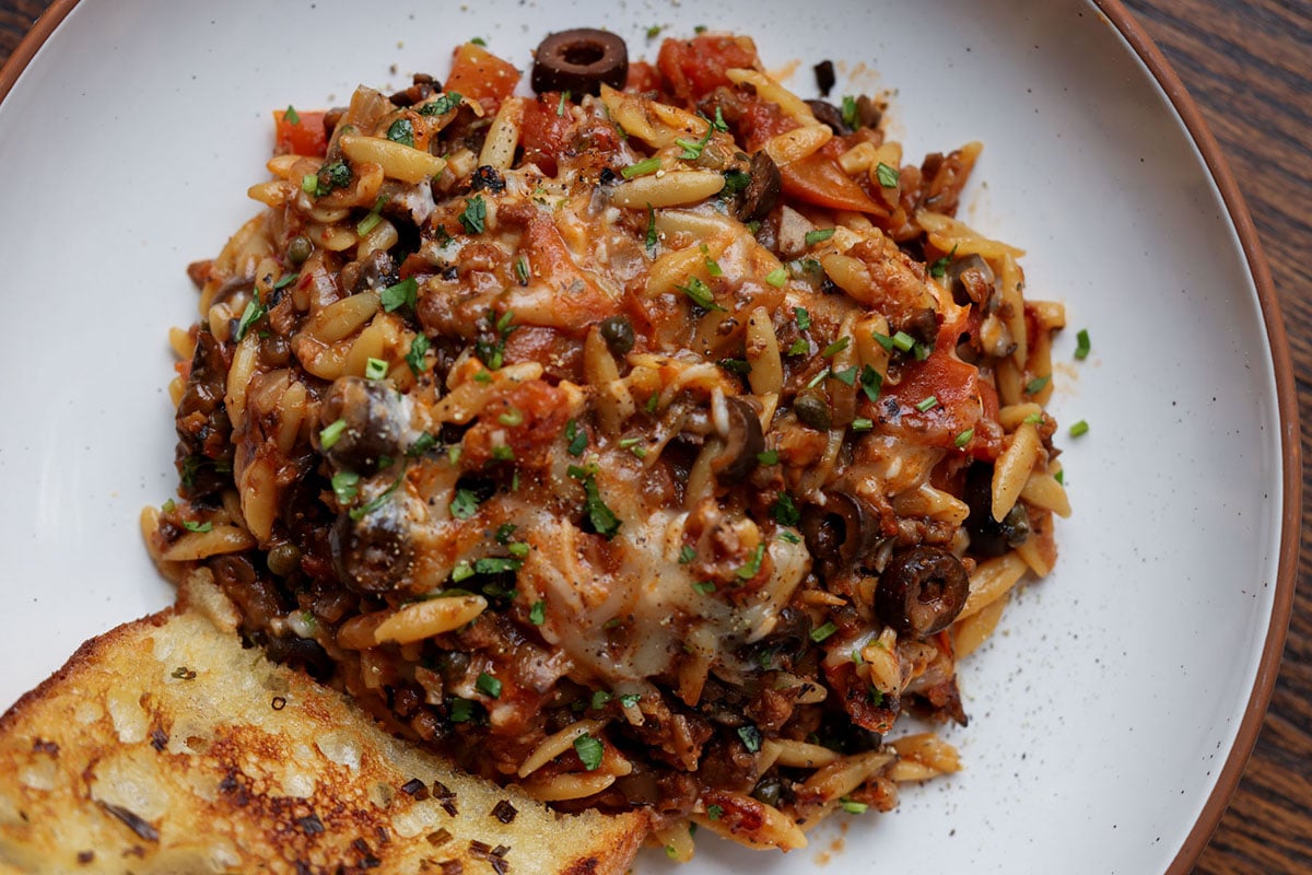 orzo puttanesca on a plate with garlic bread