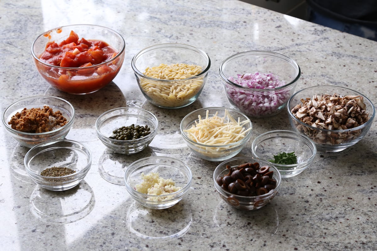 orzo puttanesca ingredients in bowls on the counter