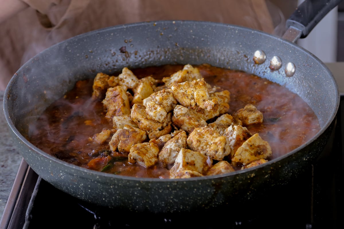 adding crisped up tofu to the Chettinad pepper chicken sauce in the pan