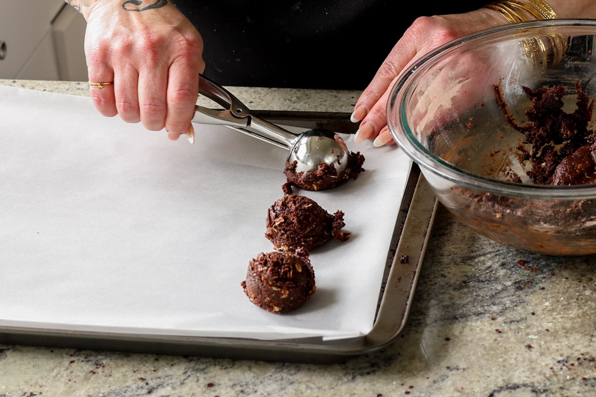 scooping cookie dough onto a lined baking sheet