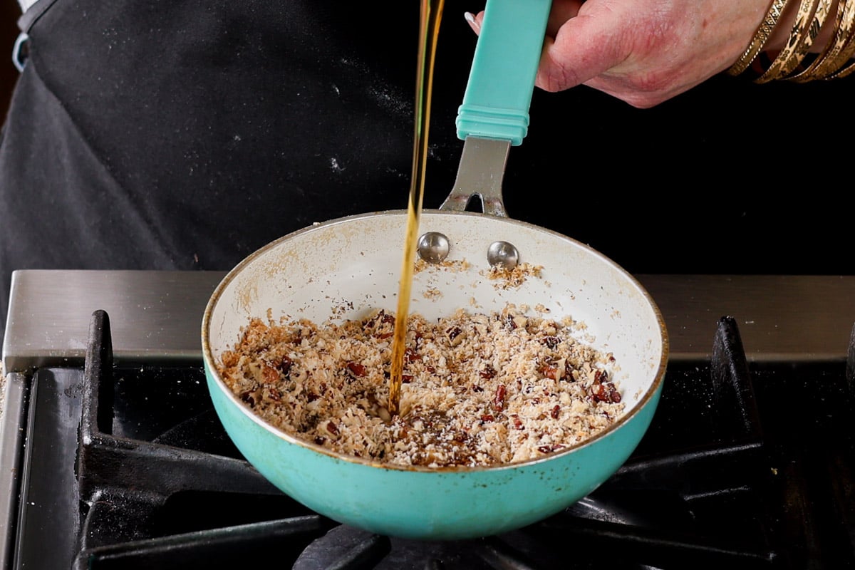 adding maple syrup to the toasted coconut and pecans in the pan