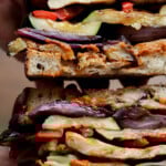 hands holding a sliced grilled veggie sandwich