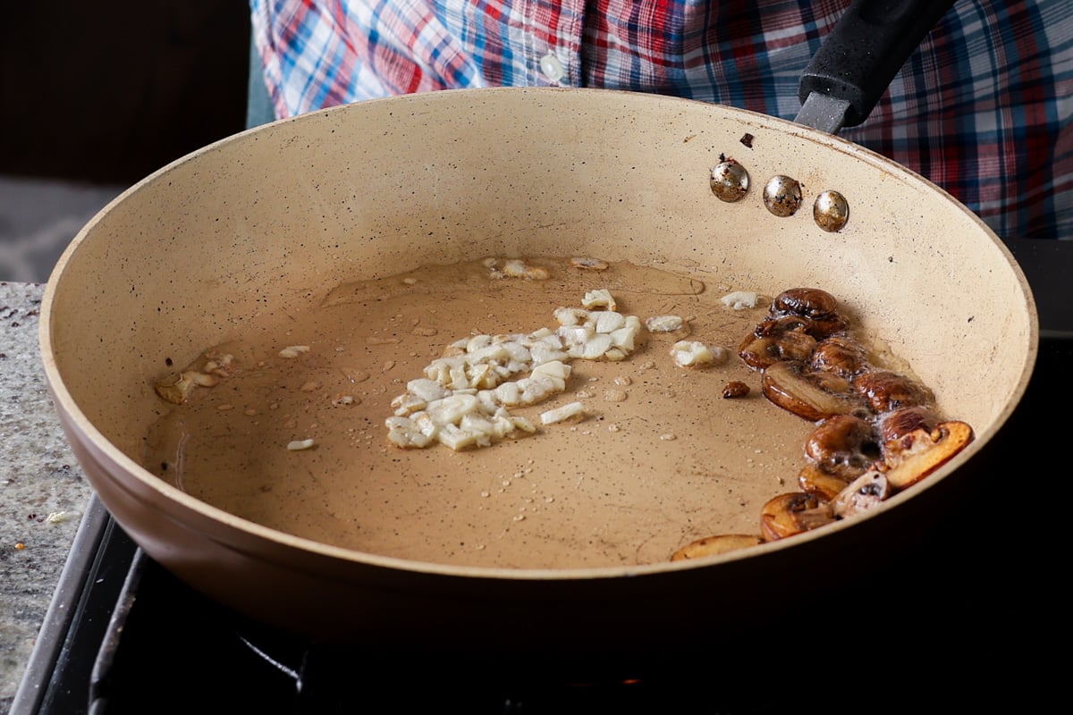 adding garlic to the pan after pushing mushrooms to the side