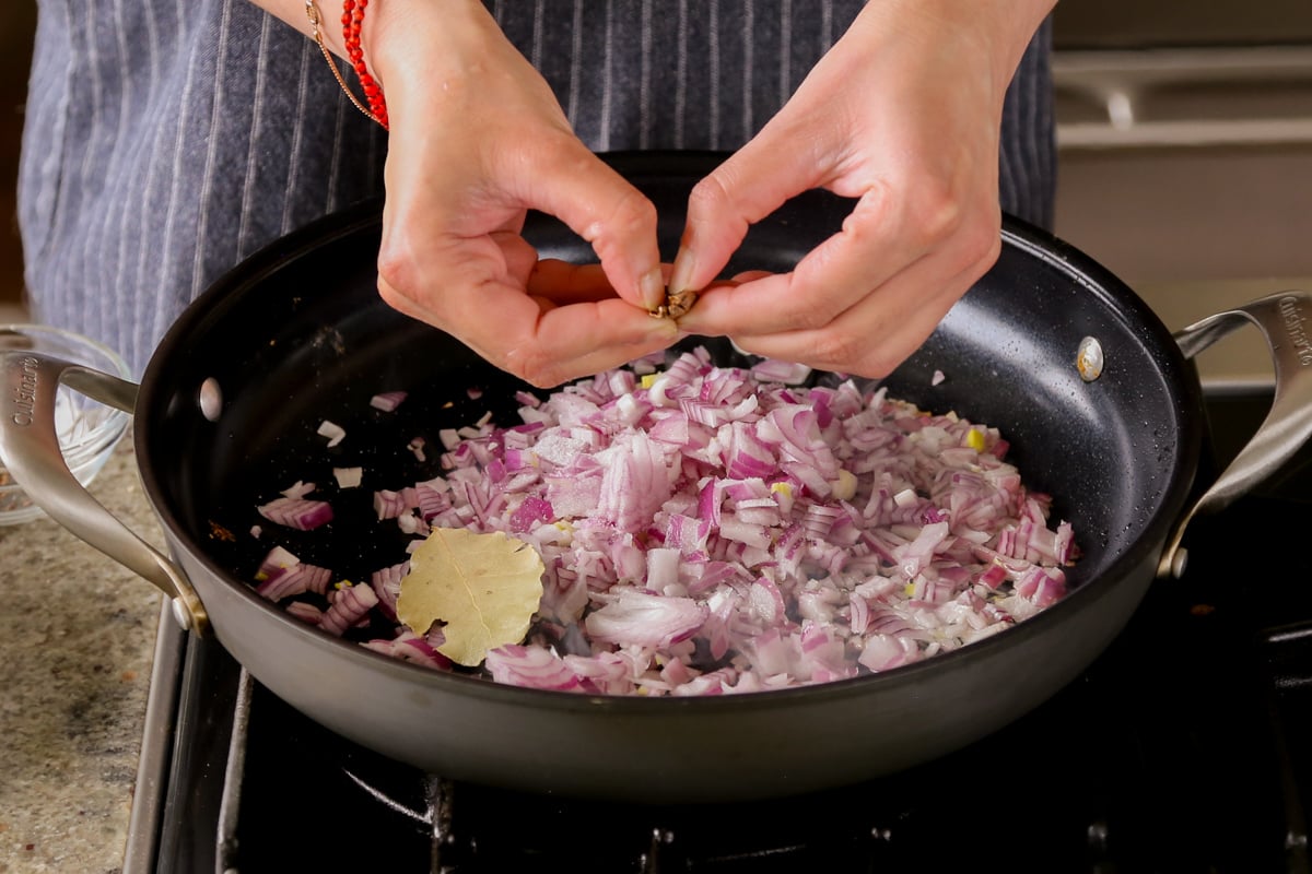 adding cardamom pod to the pan of onion and whole spices