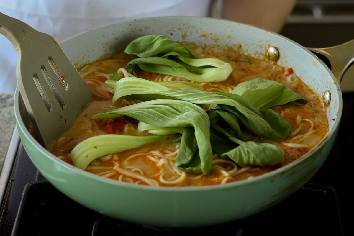adding baby bok choy to the pan of ramen noodles in tahini broth