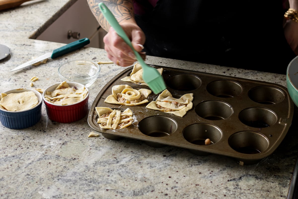 adding crust to the tops of the mini pot pies and brushing on oil before baking