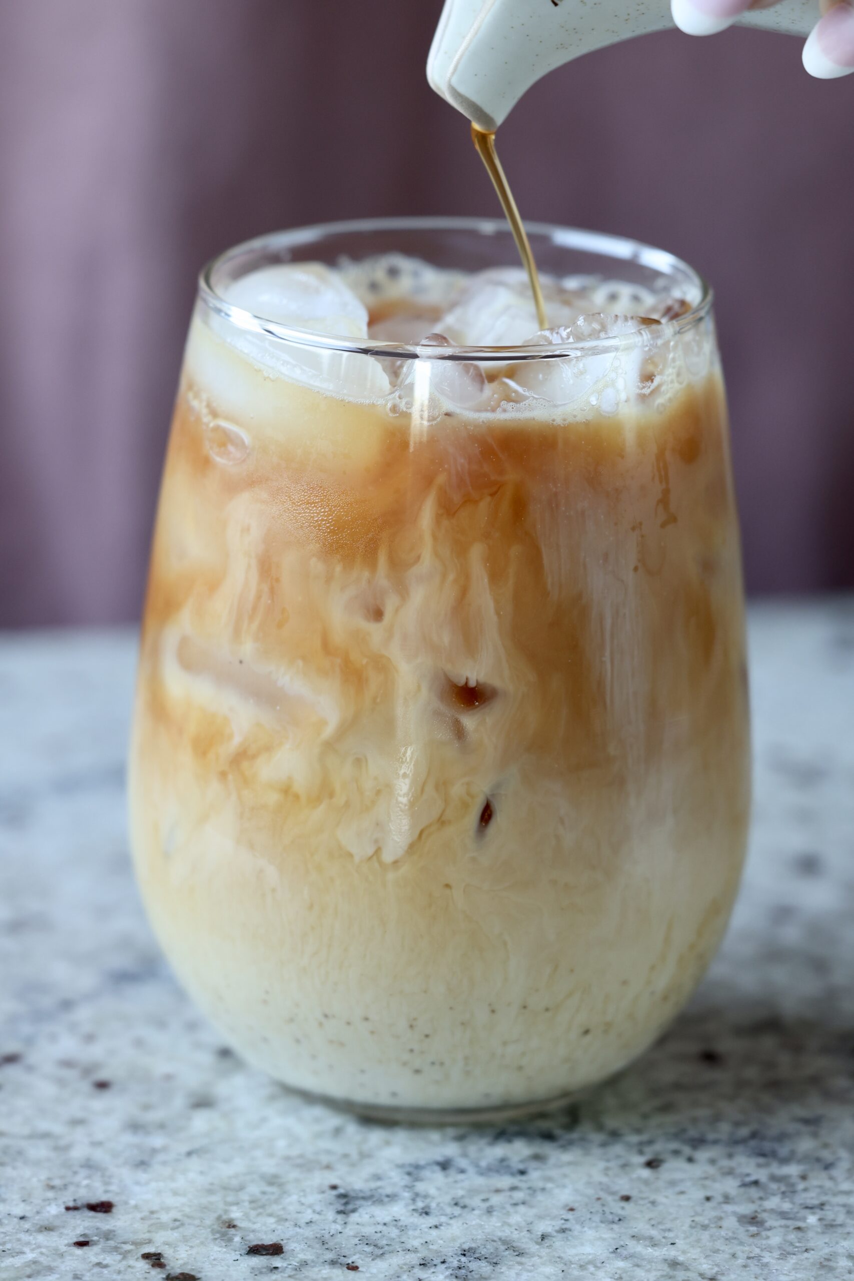 pouring chai concentrate into a glass of iced chai
