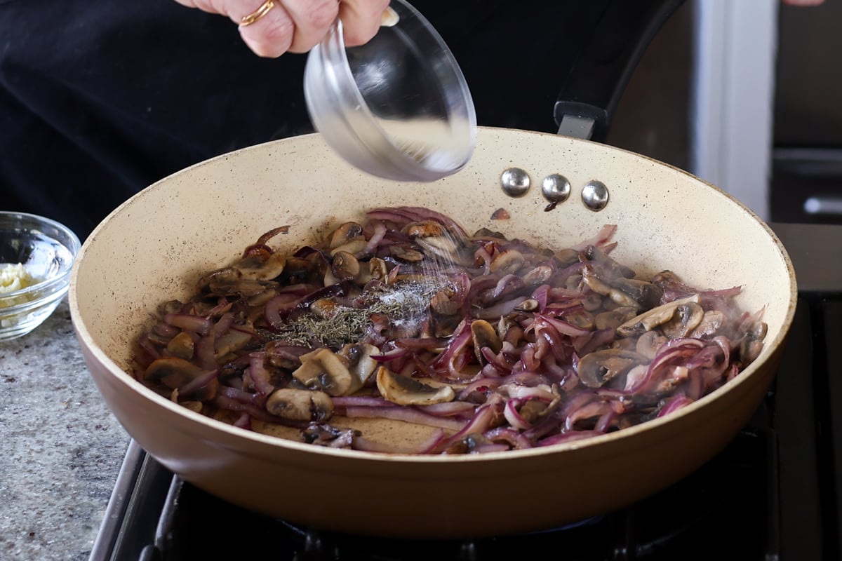 adding dried spices to the cooked mushrooms and onions