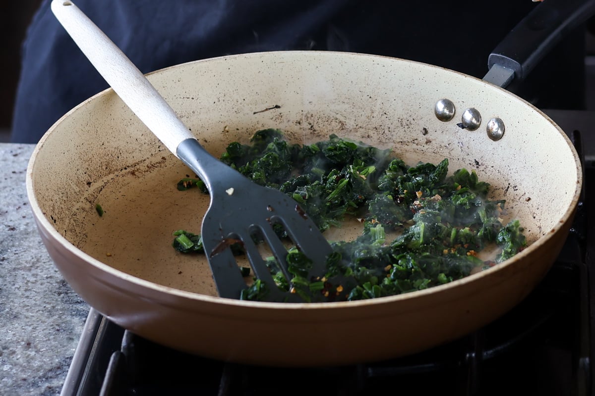 adding spinach to the garlic mixture in the pan