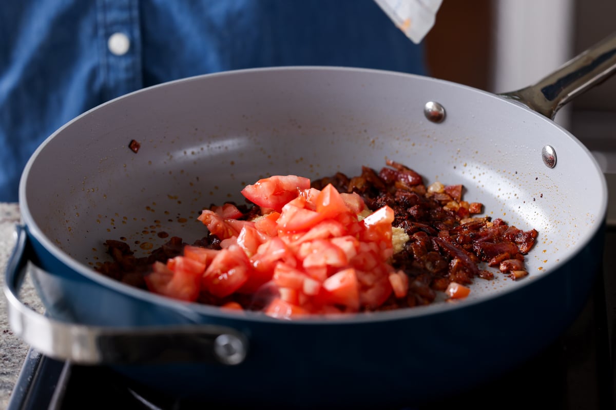 adding tomatoes to the pan