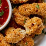 extreme close-up of vegan mozzarella sticks in a serving platter with marinara on the side with some broken sticks, so you can see the cheese