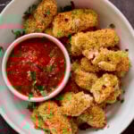 vegan mozzarella sticks in a serving platter with marinara on the side with some broken sticks, so you can see the cheese
