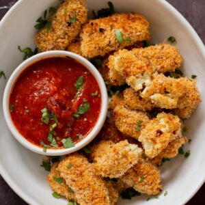 vegan mozzarella sticks in a serving platter with marinara on the side with some broken sticks, so you can see the cheese