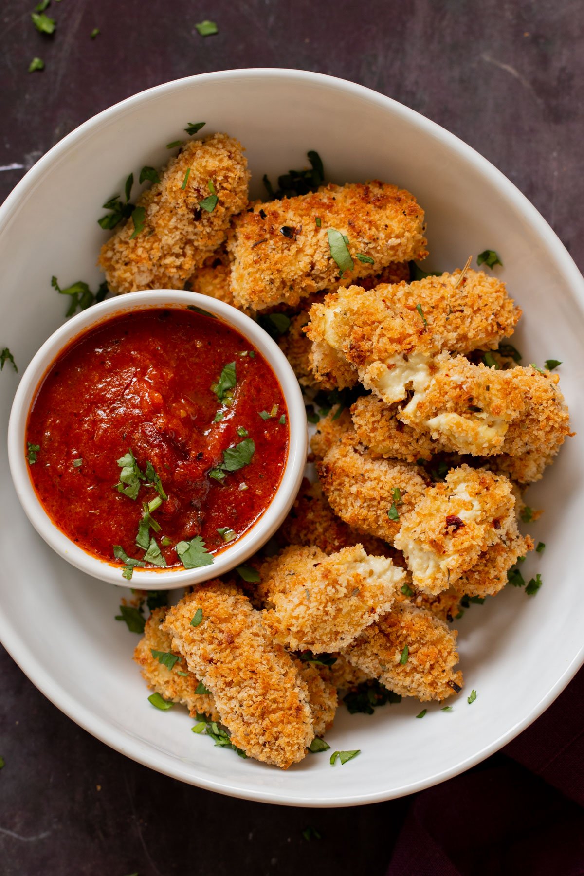 vegan mozzarella sticks in a serving platter with marinara on the side with some broken sticks, so you can see the cheese