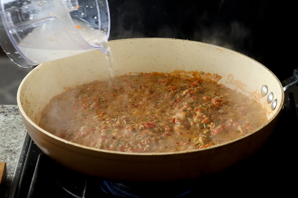 adding water to the pan of Sicilian pesto sauce