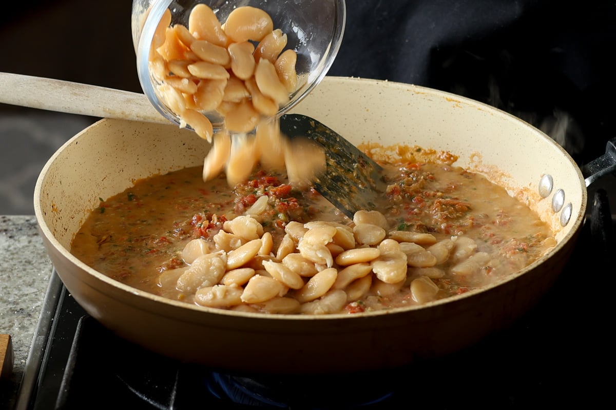 adding butter beans to the pan of Sicilian pesto sauce