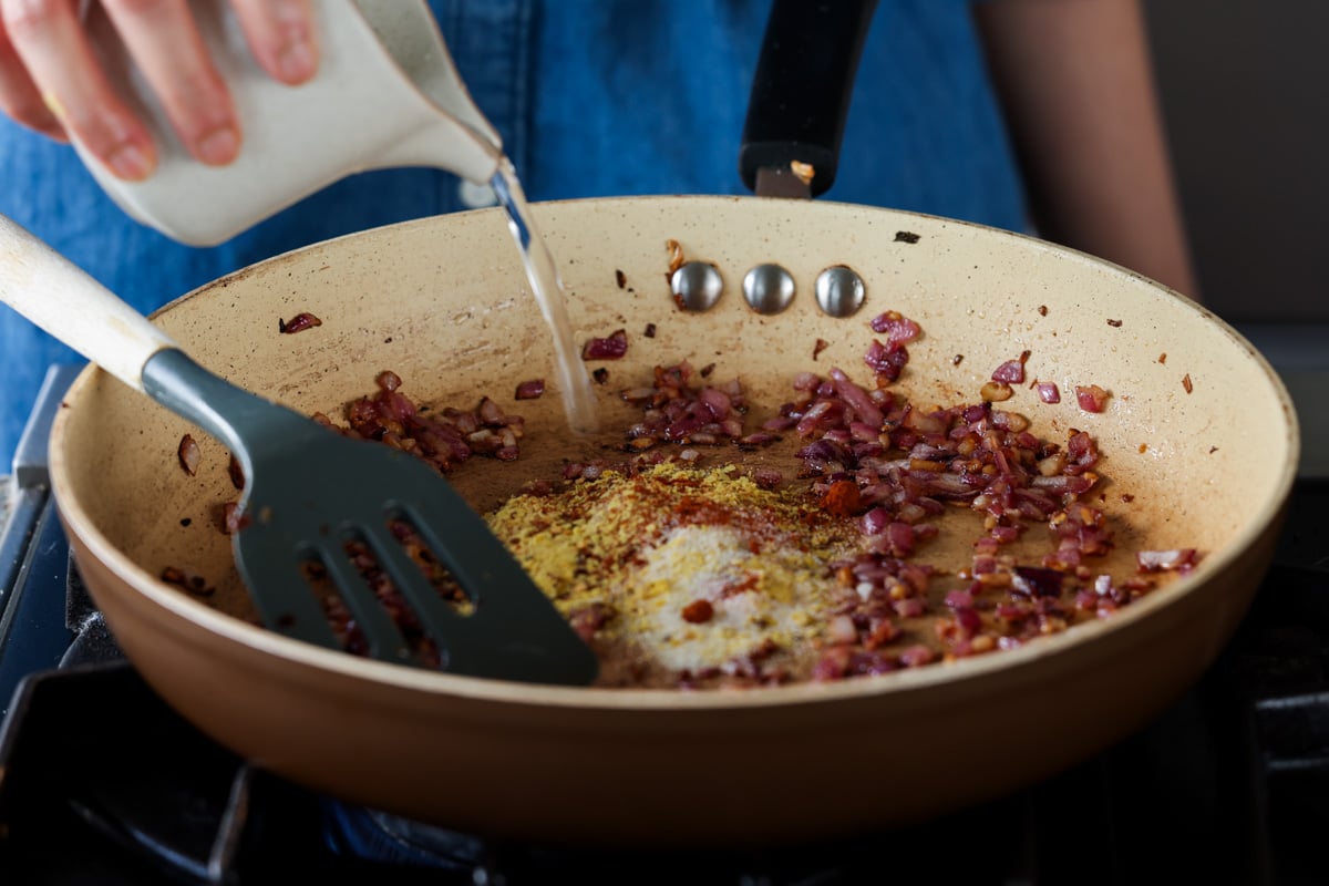adding nutritional yeast, spices, and water to the pan
