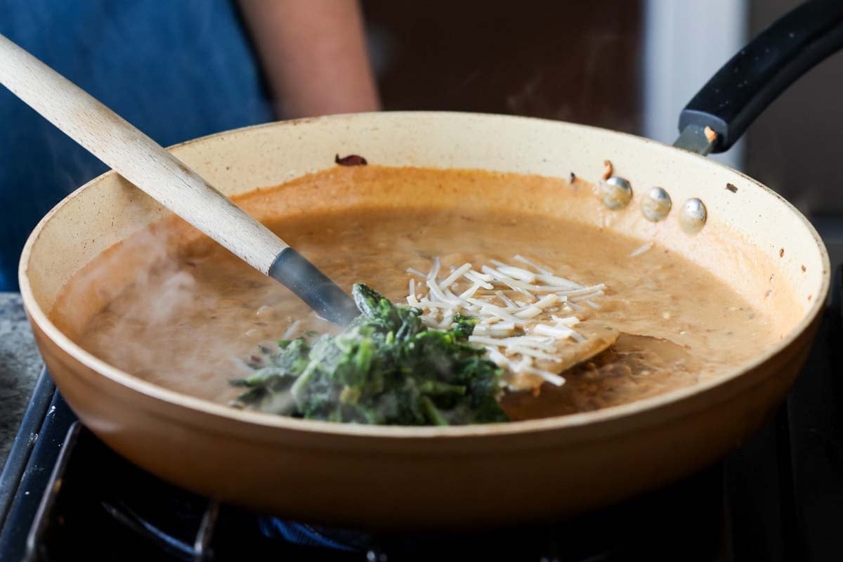 adding spinach and vegan cheese to the pan