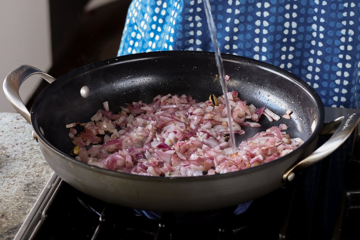 adding a splash of water to the pan of onions