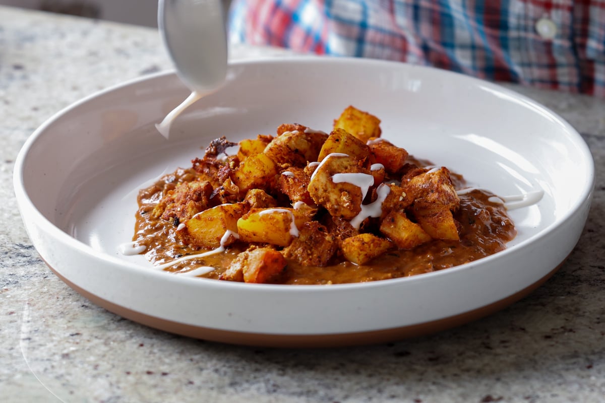 drizzling yogurt onto paneer ghee roast on a serving plate