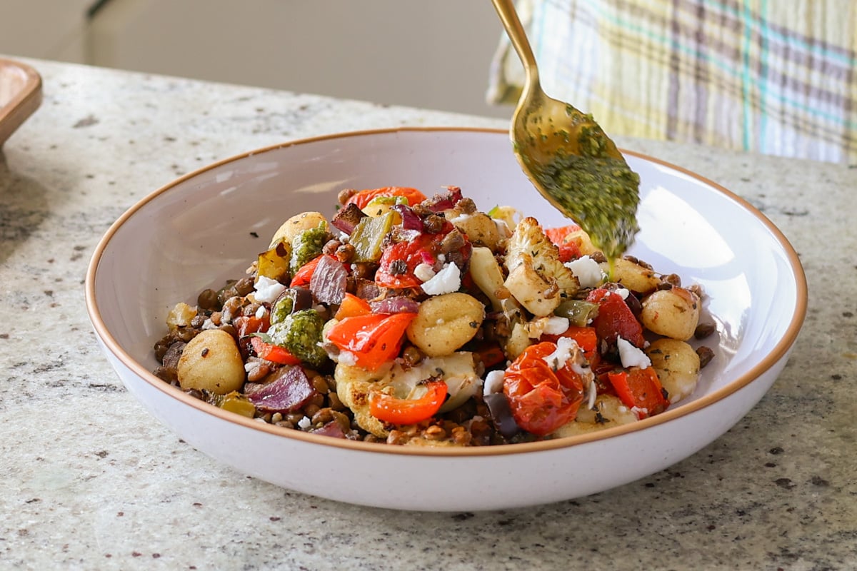 adding pesto to sheet pan gnocchi