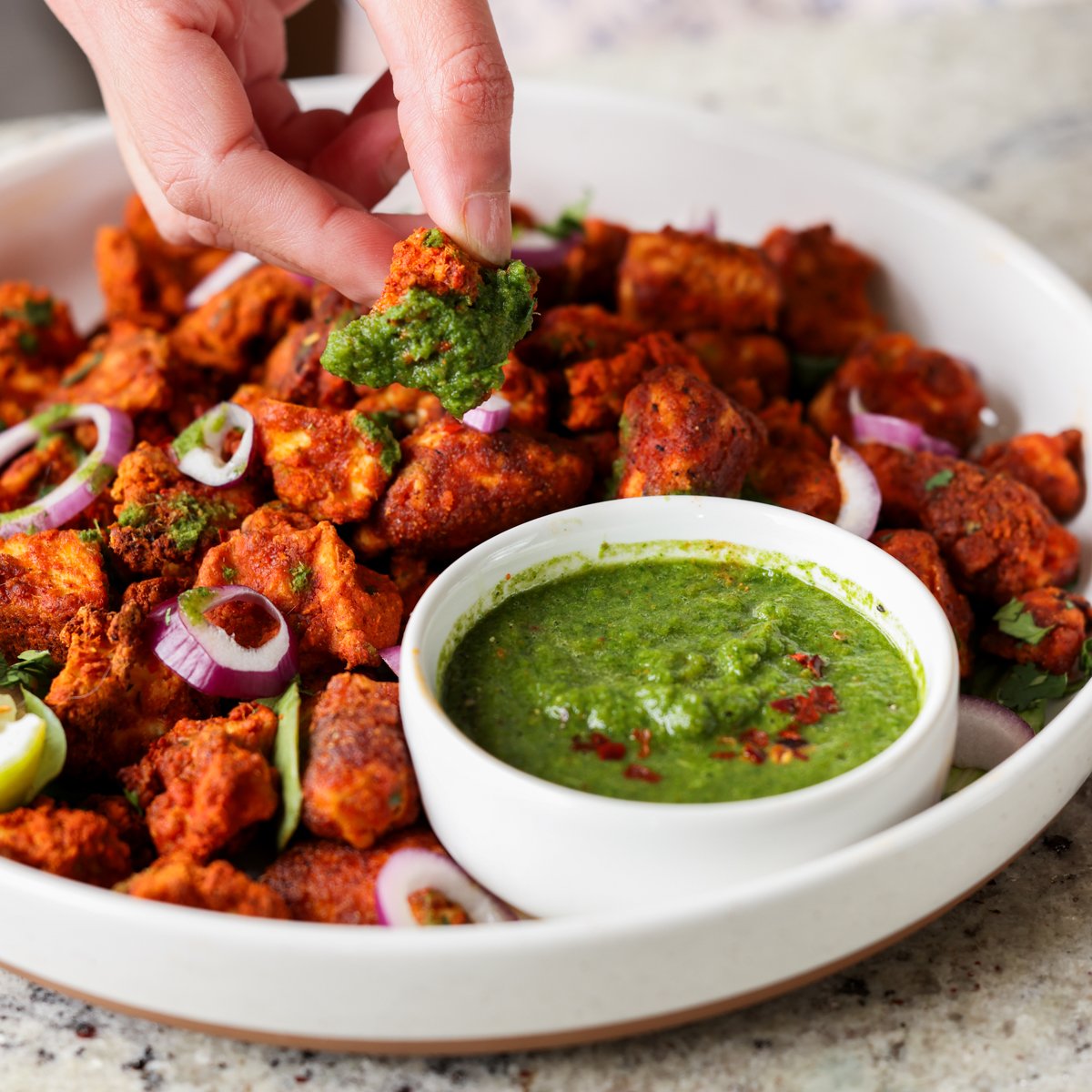 dipping a piece of tofu Koliwada into the mint chutney