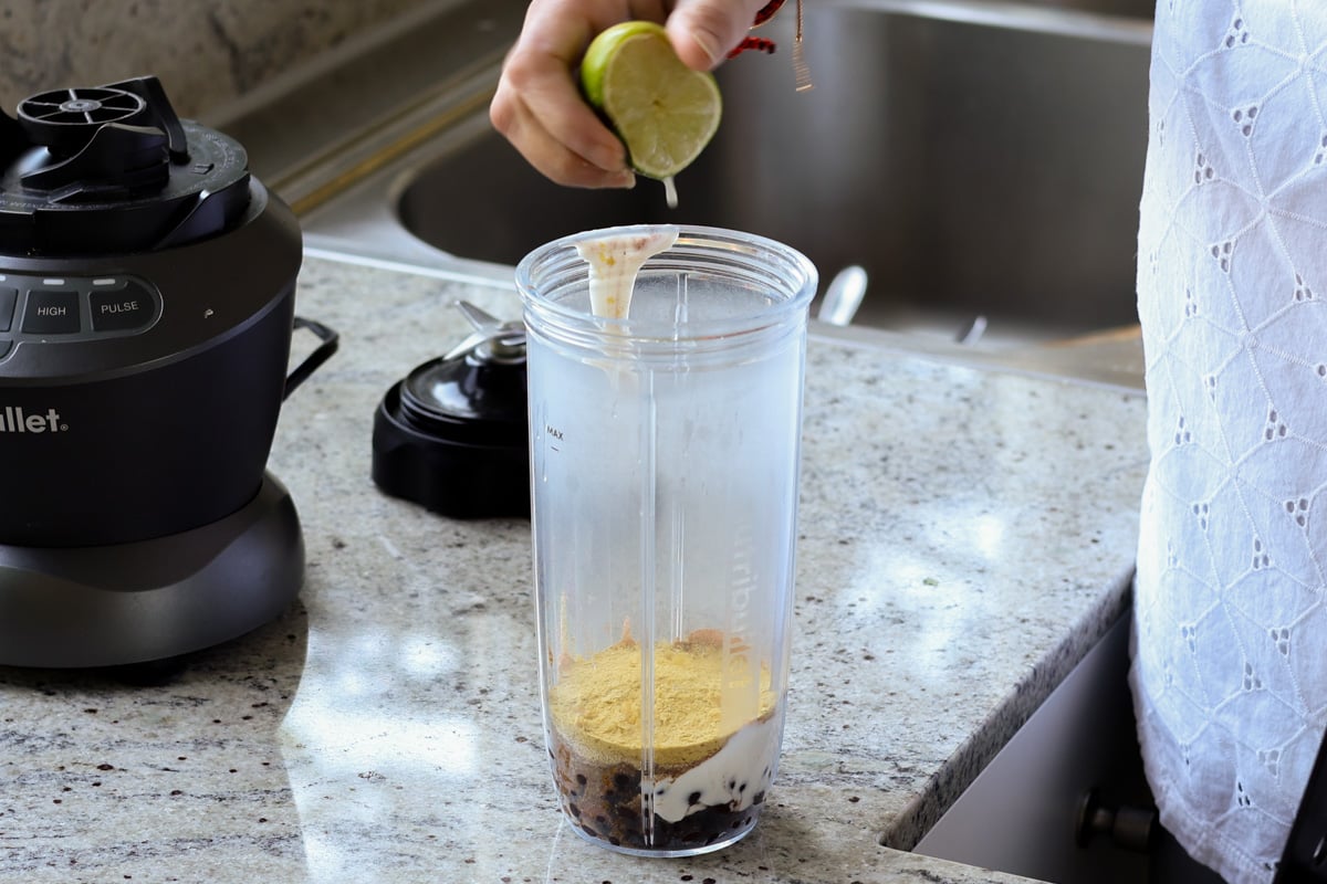 Beans, yogurt, nutritional yeast, and lime being added to the blender.