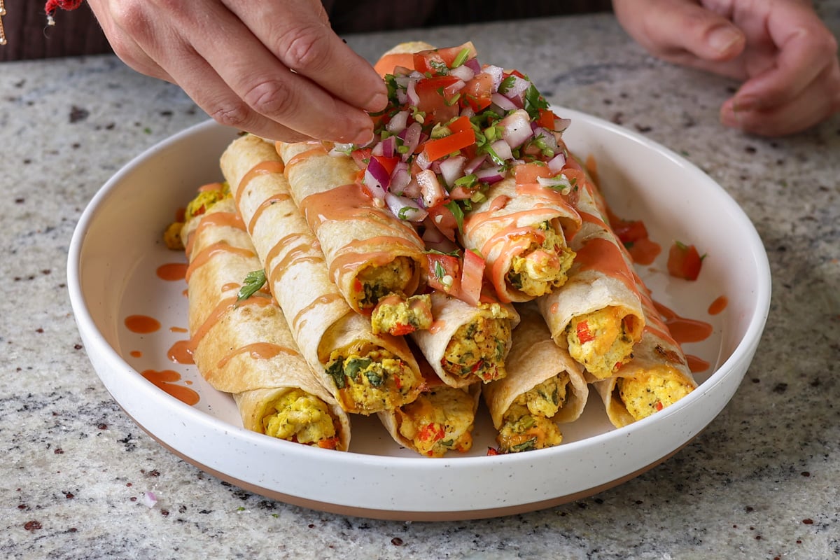 topping breakfast taquitos with pico and creamy hot sauce mixture