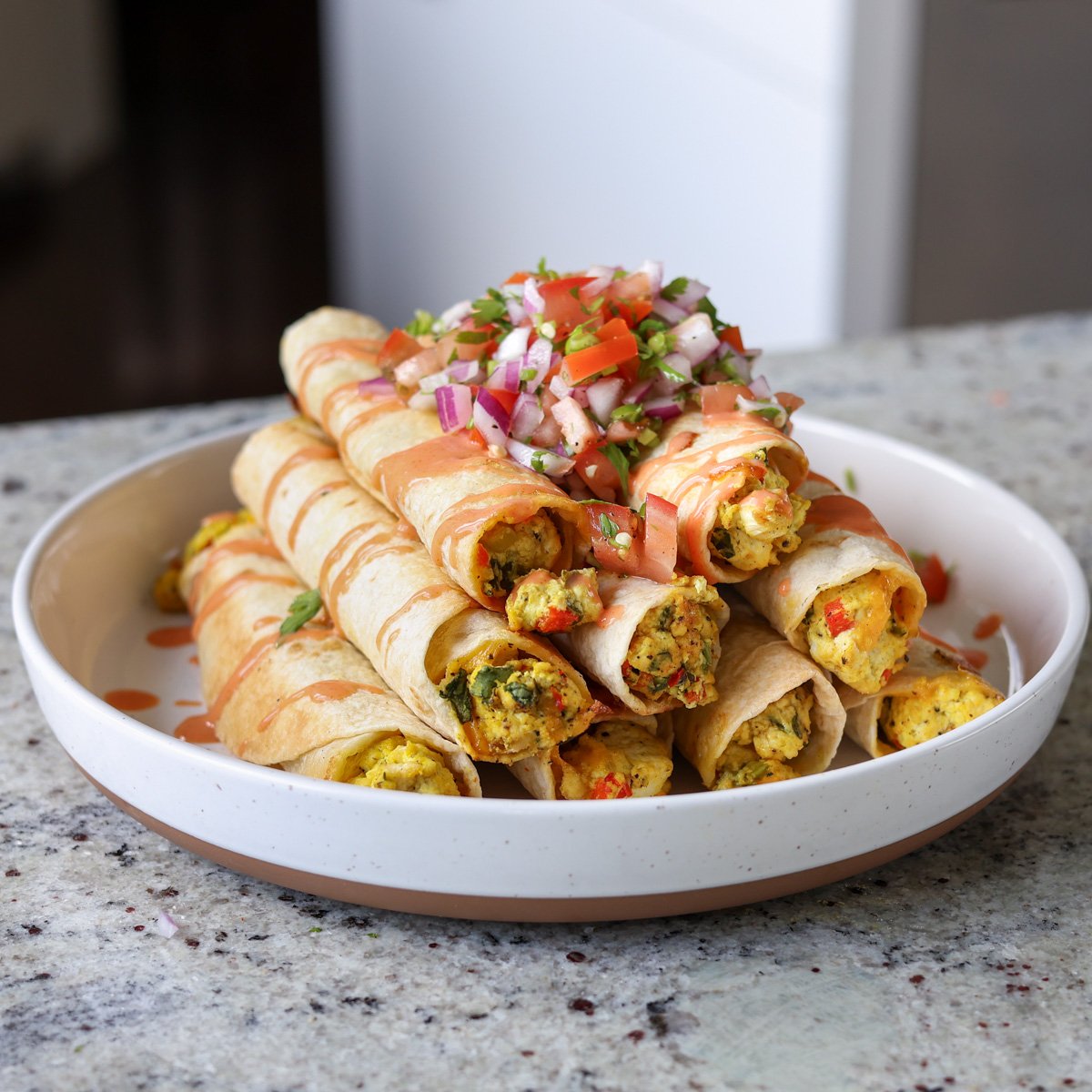 breakfast taquitos on a plate topped with pico de gallo and creamy hot sauce