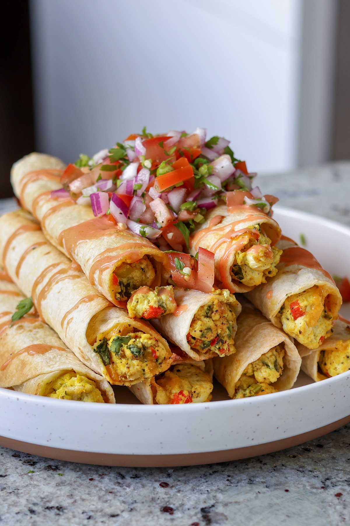 breakfast taquitos on a plate topped with pico de gallo and creamy hot sauce