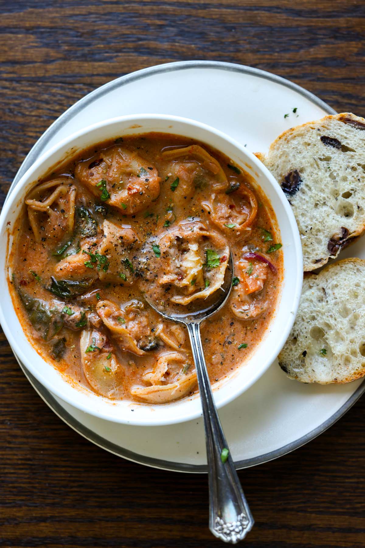 bowl of tortellini soup with a spoon and a side of bakery bread