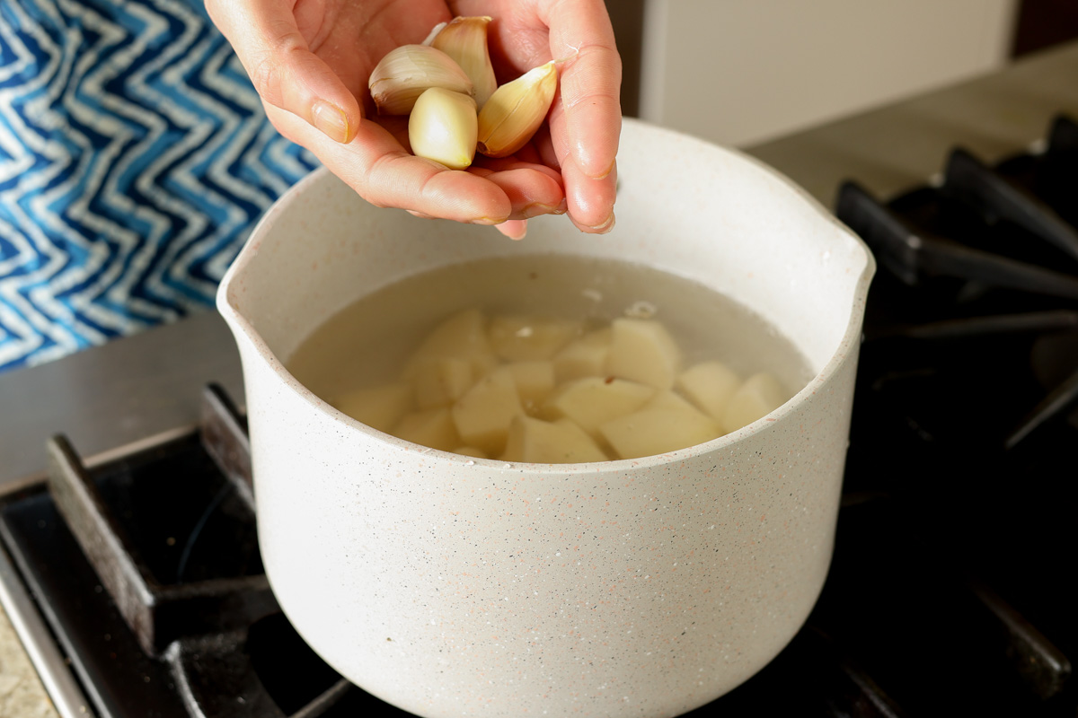 adding garlic cloves to the pan of potatoes