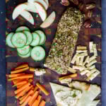 holiday cheese log on a party platter with veggies, chips, pita, and apple slices
