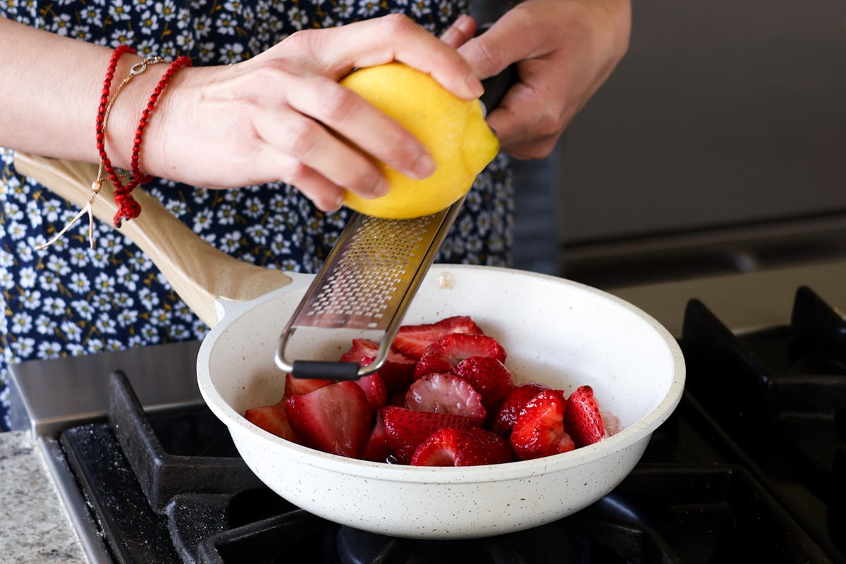 adding strawberries, maple syrup, and lemon zest to a pan