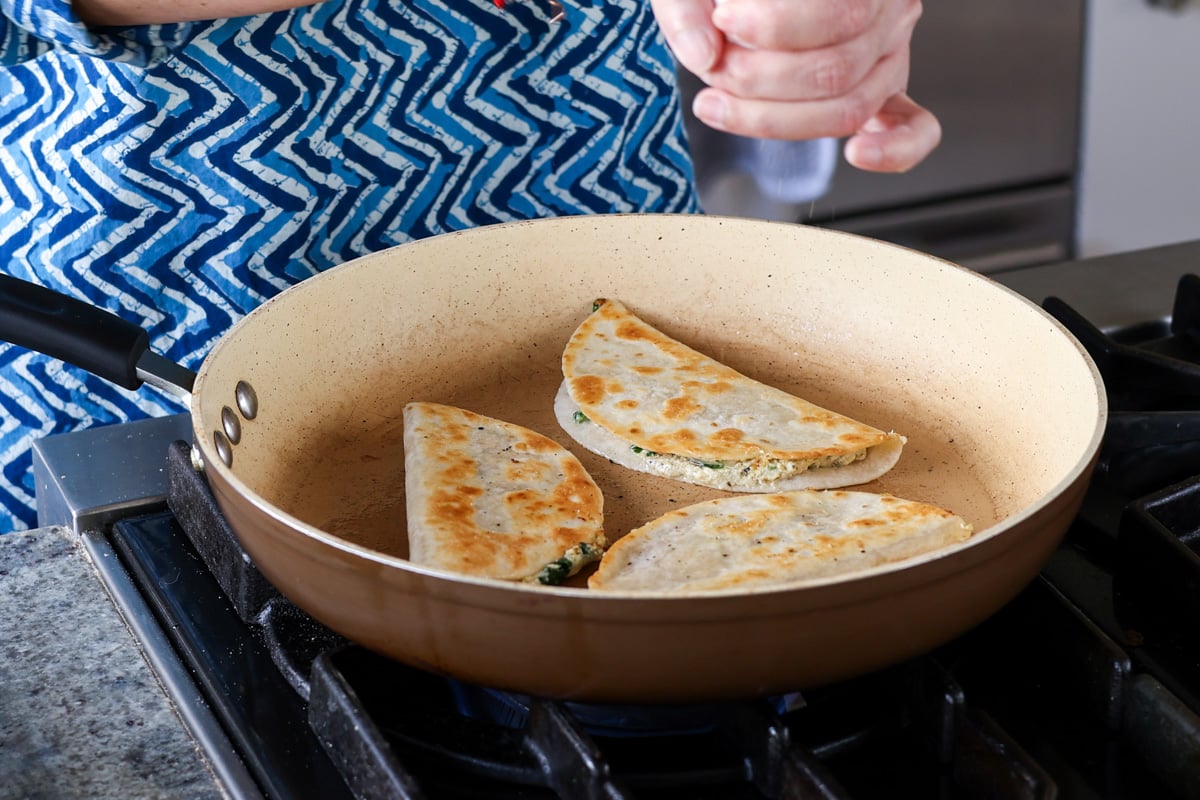 adding black pepper to the crispy tacos in the pan